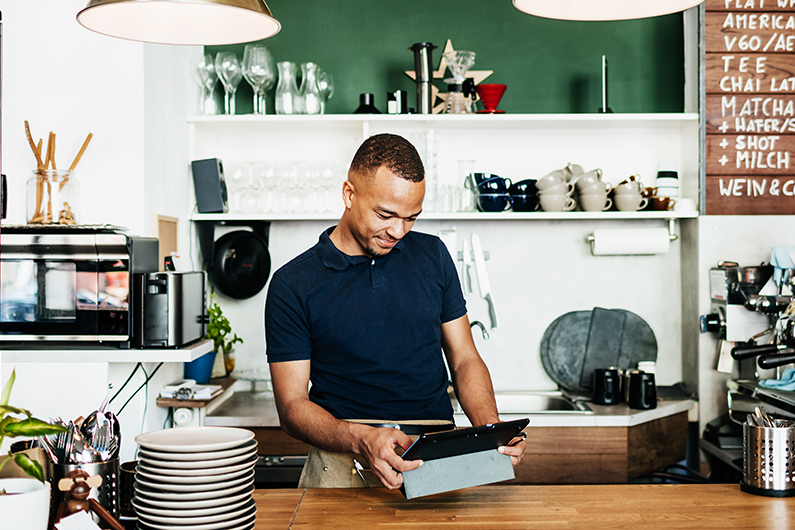 A male coffee shop owner using a digital tablet at the service counter.