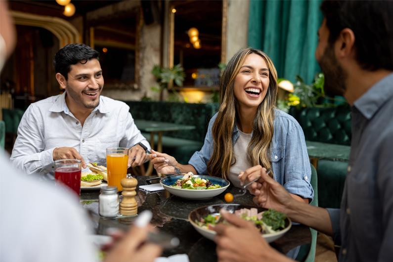 Group of friends dining at a restaurant, illustrating how meals and social outings are common expenses to consider putting on a credit card.