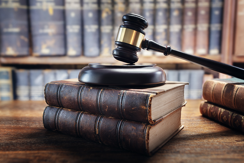 Gavel resting on a sound block placed on top of two stacked books, with shelves of books blurred in the background.