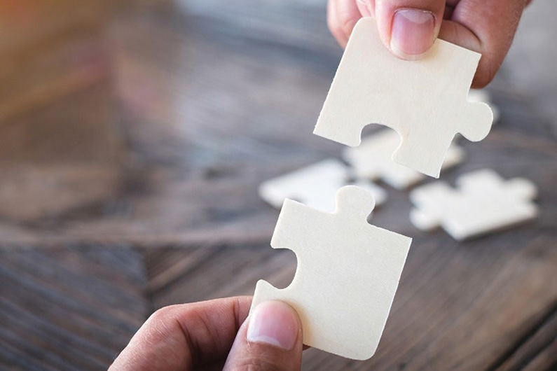 A set of hands holding two white puzzle pieces.