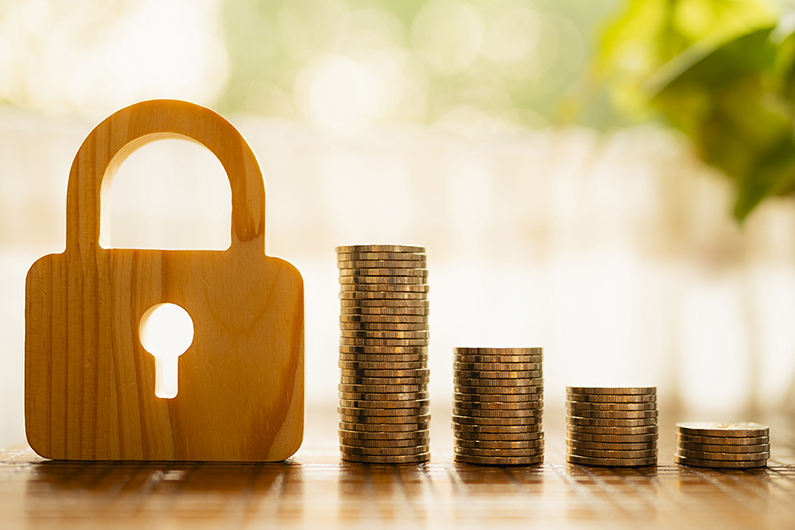  A wooden padlock figure placed next to four stacks of coins arranged in ascending order on a wooden surface, with a blurred green and white background suggesting natural light.