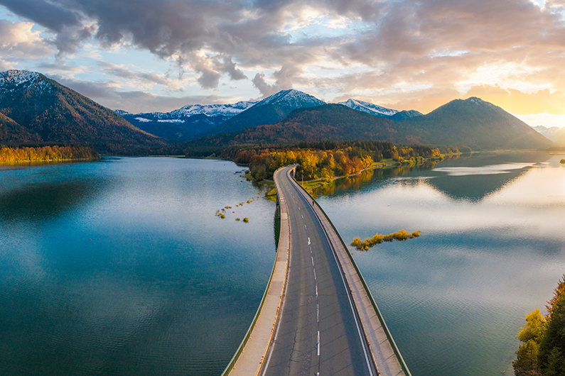 A paved highway bridge over a body of water with mountains in the background at sunset.