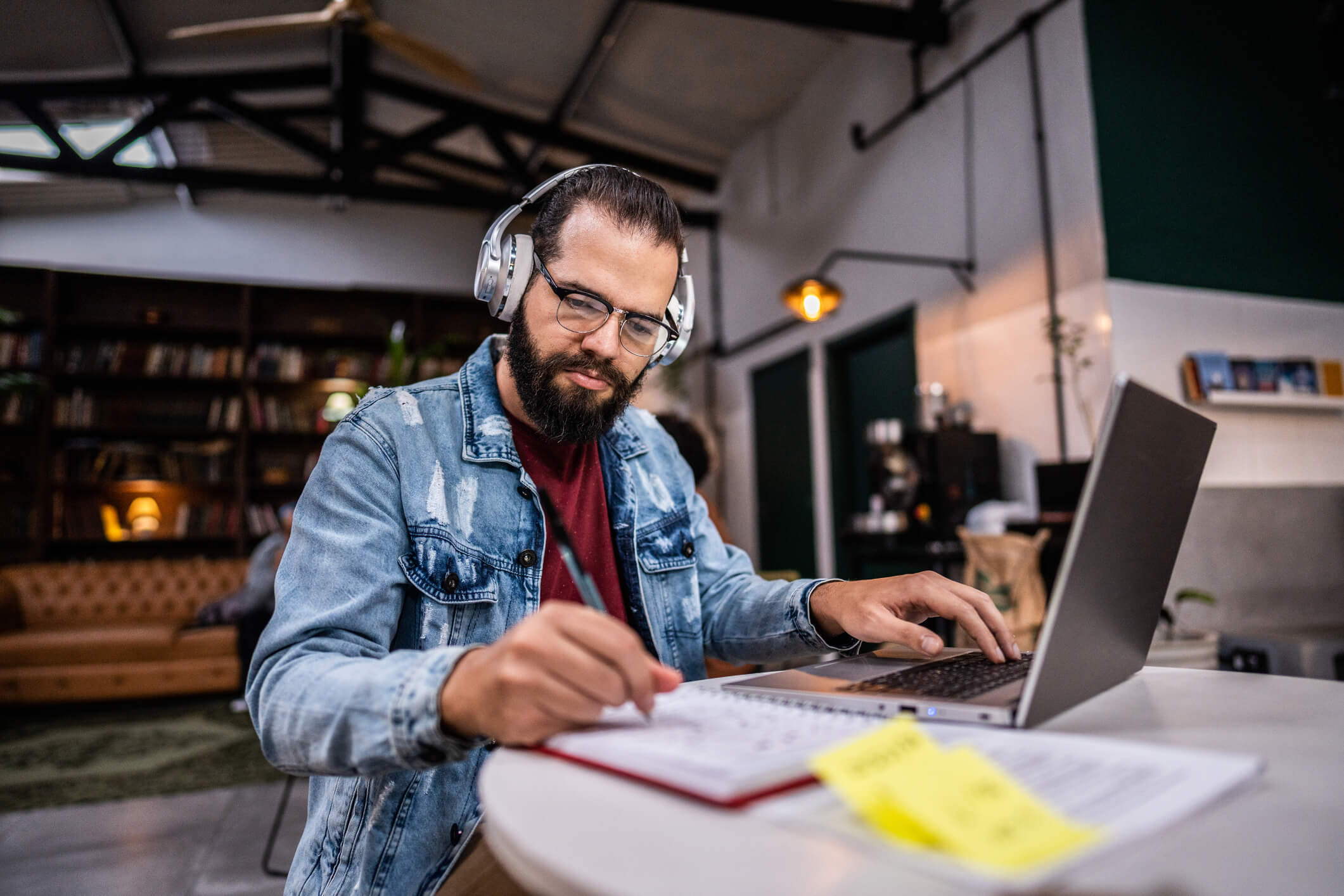 A man sits at a table, working on a laptop, with headphones on. 