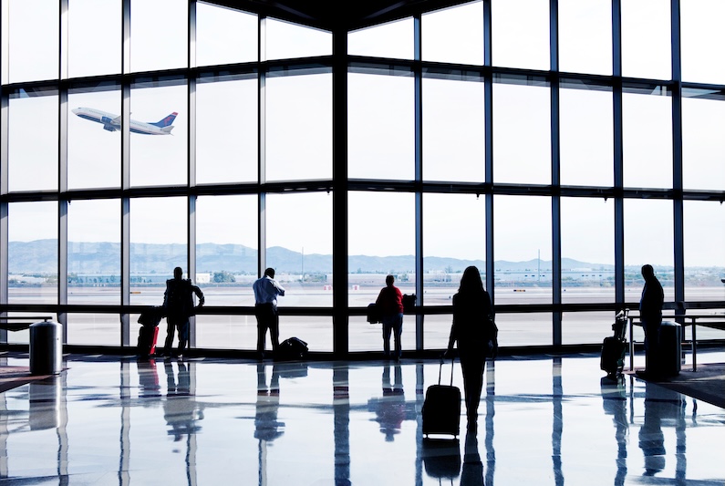 A group of passengers stand near a large glass window at an airport terminal.