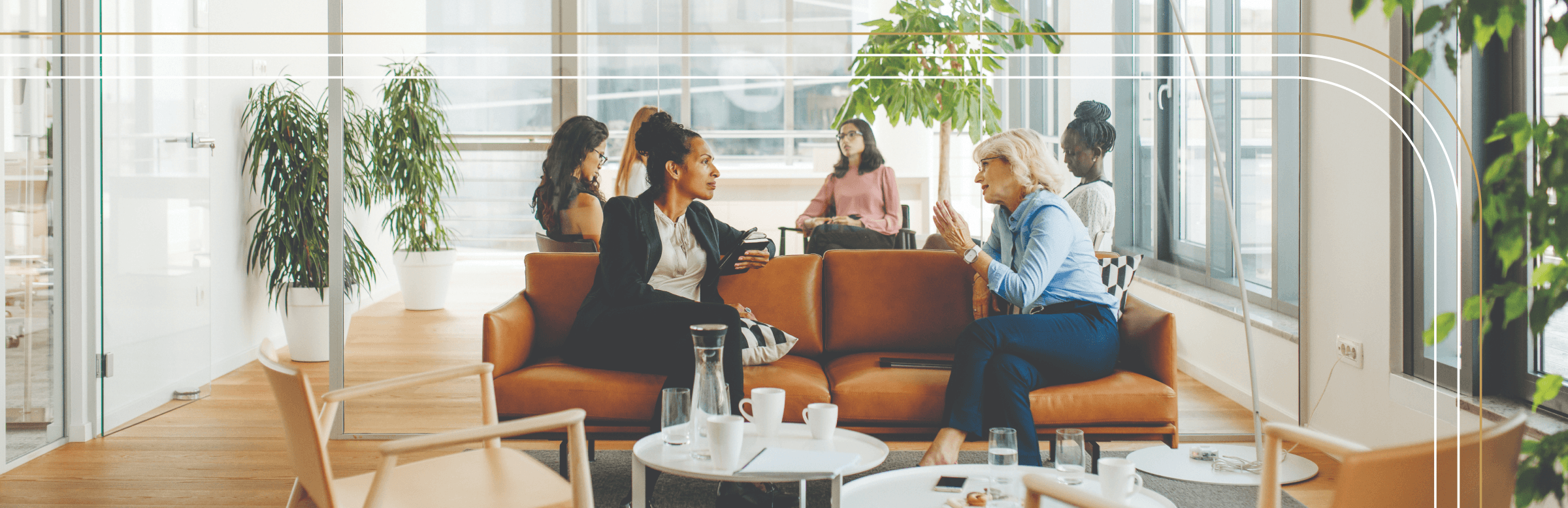 Scene of six women in a room in an office building, in a casual setting, talking 