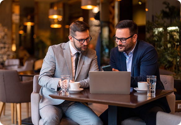  Two adult men sitting in a coffee shop looking at a computer